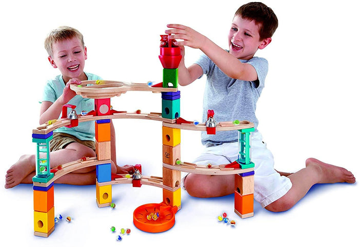 Two boys play with a colorful wooden marble run featuring curved tracks, bells, vibrant blocks, and glass marbles.
