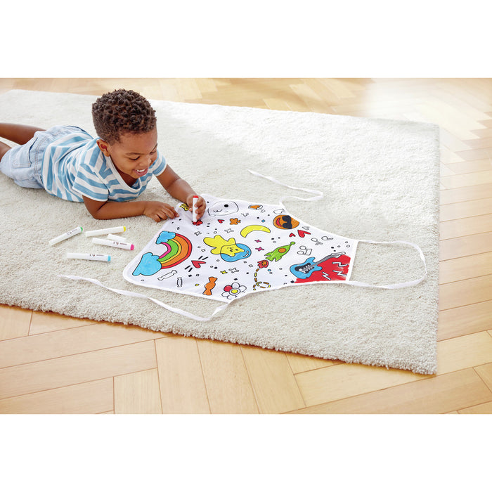 Child coloring a white art apron with black-line drawings of a rainbow and guitar using markers on a rug.