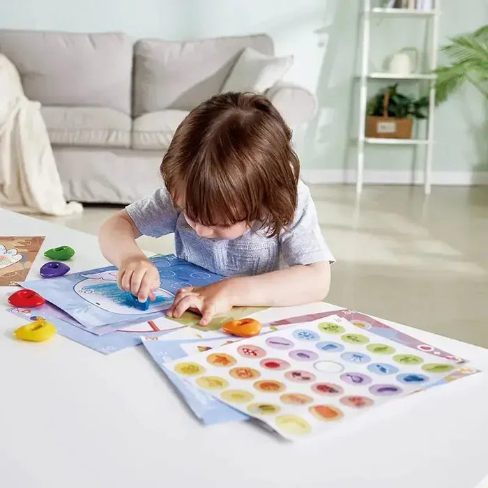 A child uses colorful pebble-shaped crayons to color sea-themed activity sheets at a bright white table.