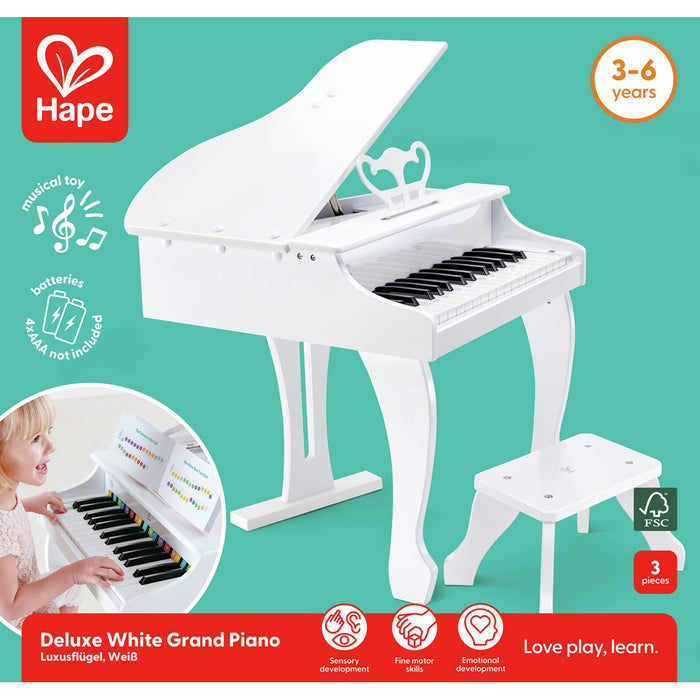White toy grand piano with matching stool and music stand. Teal background shows brand logos and a child playing.