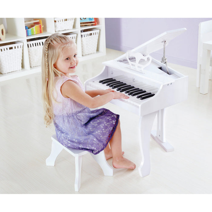 Child playing a white wooden toy grand piano with an open lid, music stand, and matching stool.
