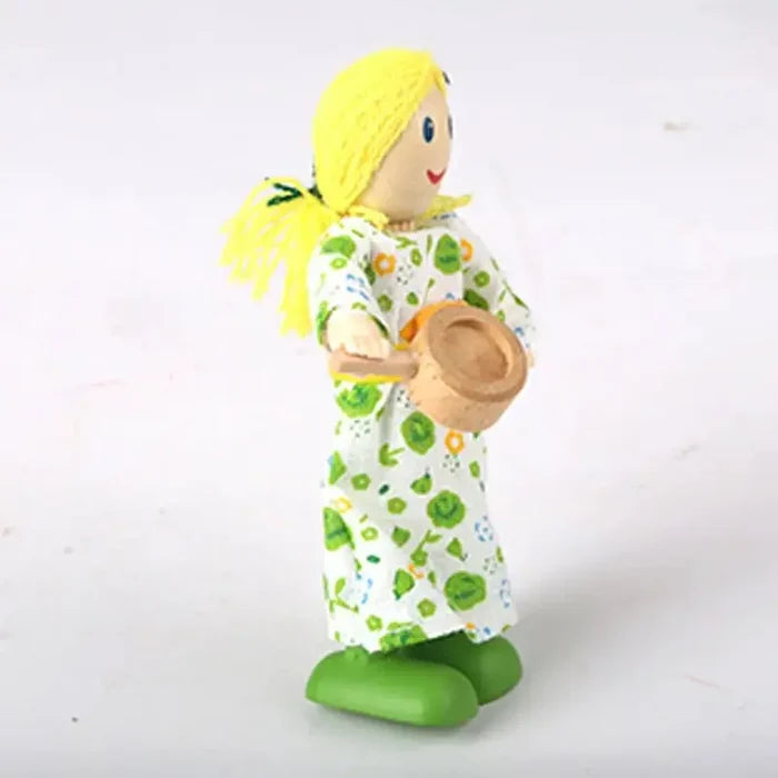 Small wooden doll with yellow yarn hair, a green floral dress, and green shoes holding a wooden frying pan.