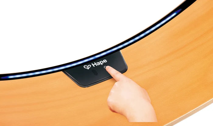 Finger pressing a power button on a curved wooden balance board with a glowing blue LED strip along its edge.