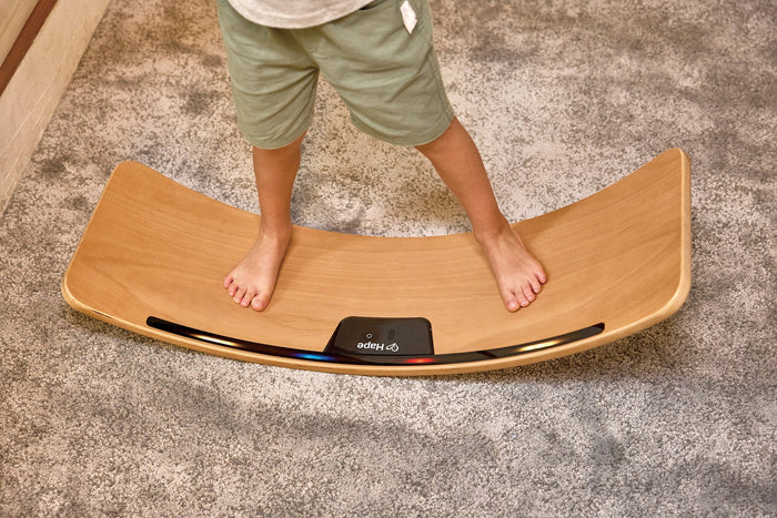 Child on a curved wooden balance board featuring a black center panel and glowing blue and red lights along the edge.