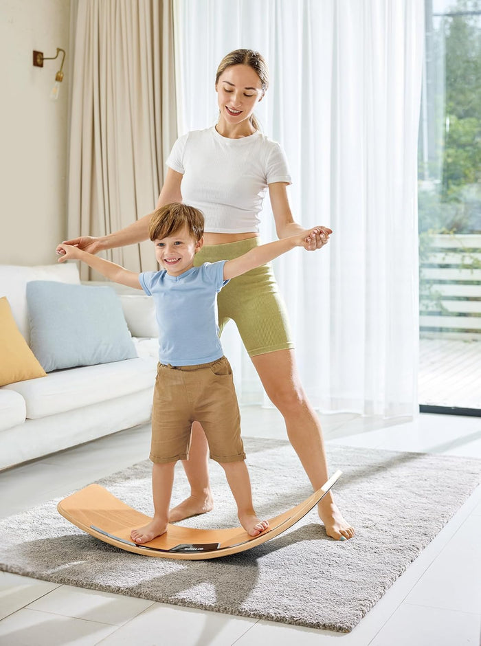 Boy on a curved light-wood balance board with a central light strip, assisted by a woman in a bright room.