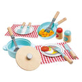 Wooden toy cooking set with blue pots, pans, utensils, salt and pepper shakers, and toy food on checkered napkins.