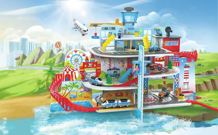 Colorful multi-level toy city with railway tracks, airport tower, crane, and elevator against a seaside backdrop.