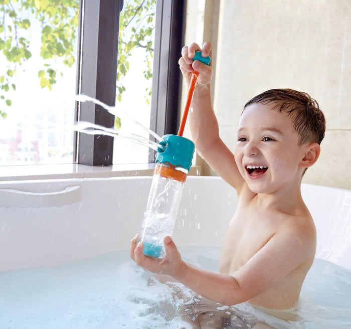 Toddler in a bathtub pumping a teal and orange water sprayer toy that shoots multiple streams of water into the air.