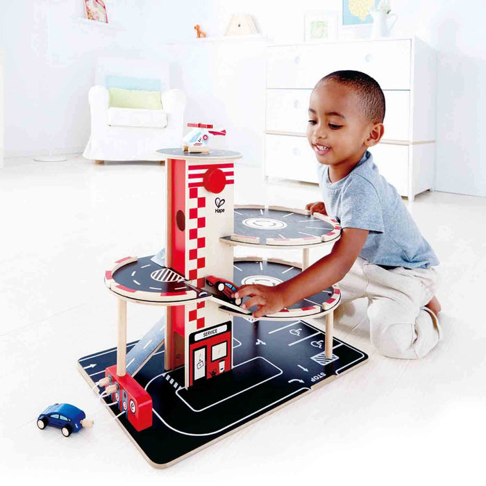 Young boy playing with a multi-level wooden toy garage featuring circular black decks and a red elevator.