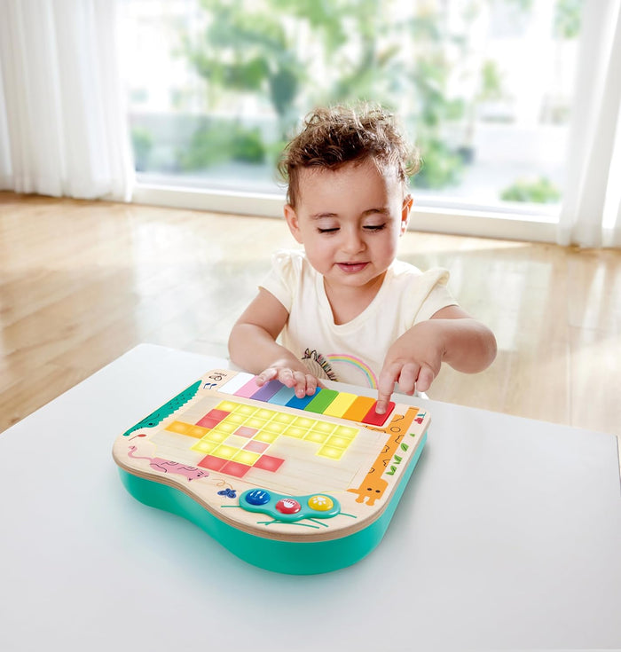 Toddler playing a colorful wooden pixel piano with rainbow keys and a glowing light-up grid on a teal base.