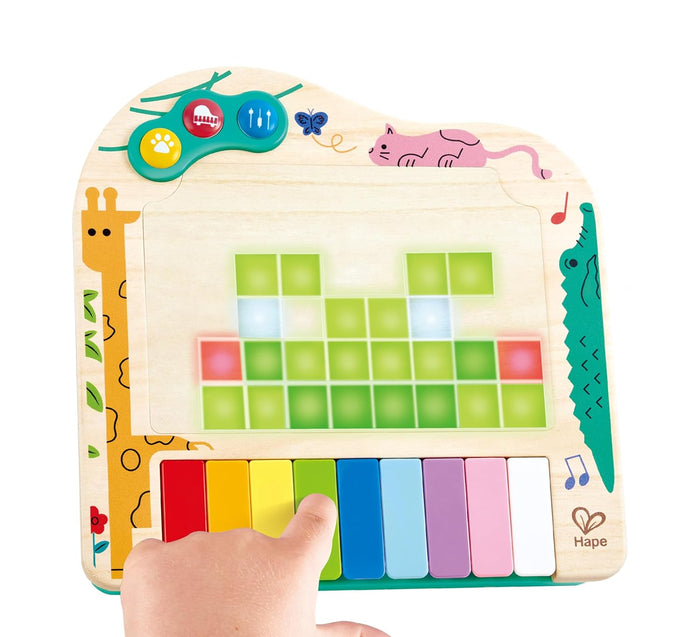 Child playing a wooden toy piano with rainbow keys and a screen displaying a glowing green pixelated frog face.
