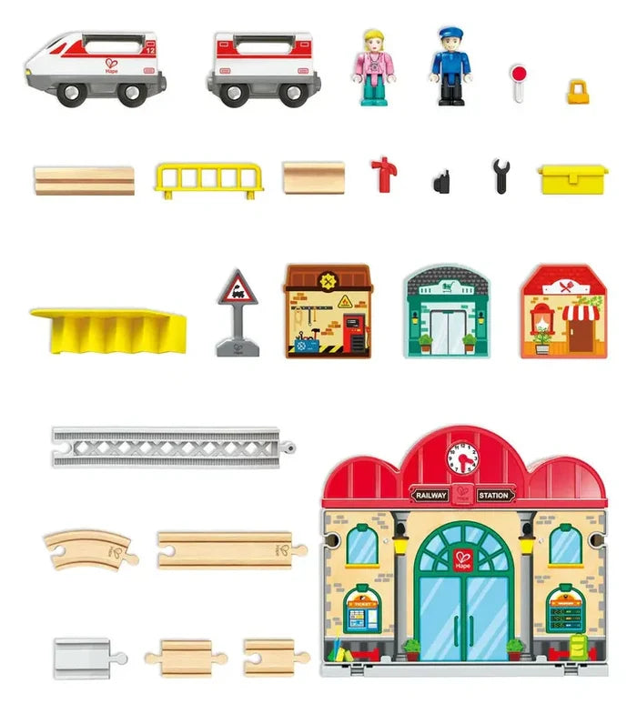 Toy train set featuring a red railway station, white train cars, figures, wooden tracks, and three small buildings.