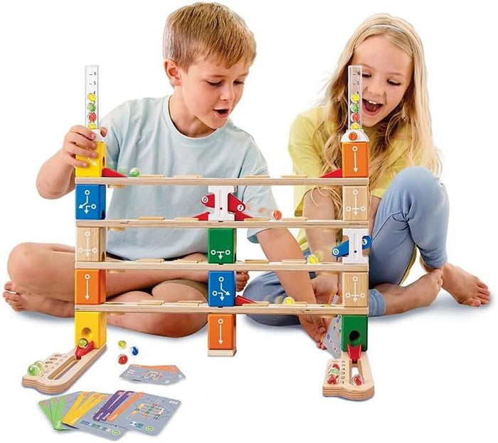 Two children playing with a multi-level wooden marble run featuring colorful blocks, tracks, and glass marbles.