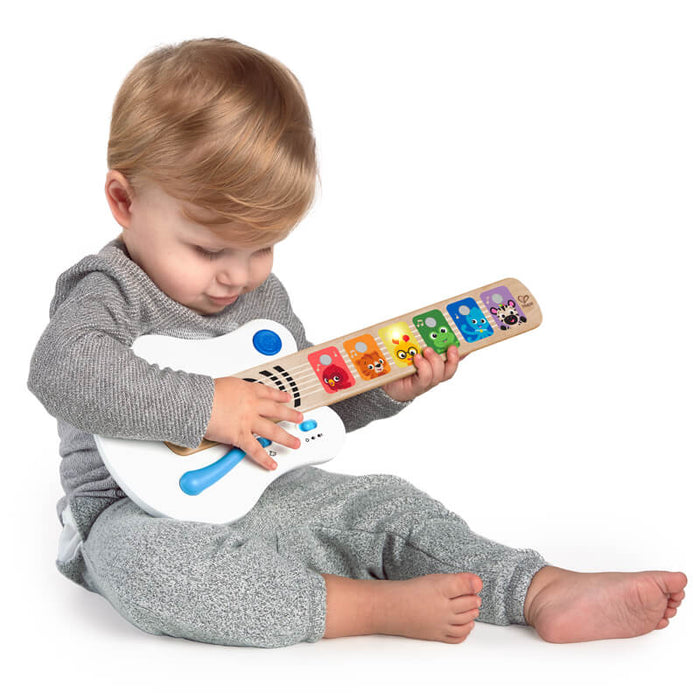 Toddler plays with a white and wood toy guitar featuring colorful light-up animal icons on the neck.