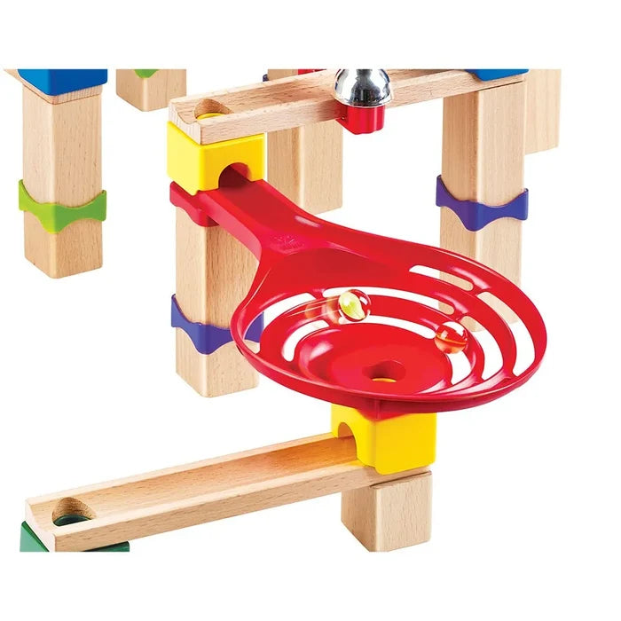 Close-up of marbles spinning in a red plastic funnel on a wooden marble run with colorful connector blocks.
