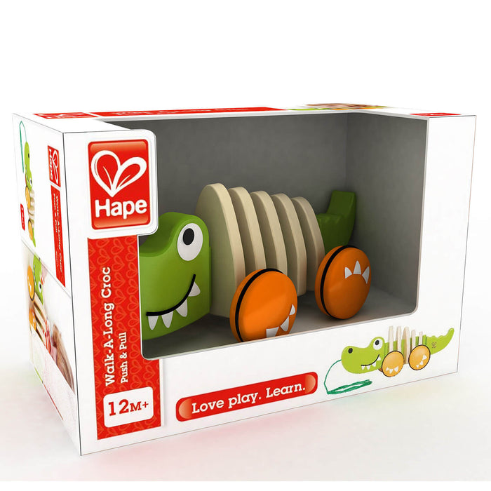 Wooden green crocodile pull toy with segmented body and orange wheels in its white and red retail box.