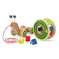 Wooden snail pull toy with big eyes, red string, and a removable green shape sorter shell with colorful blocks.