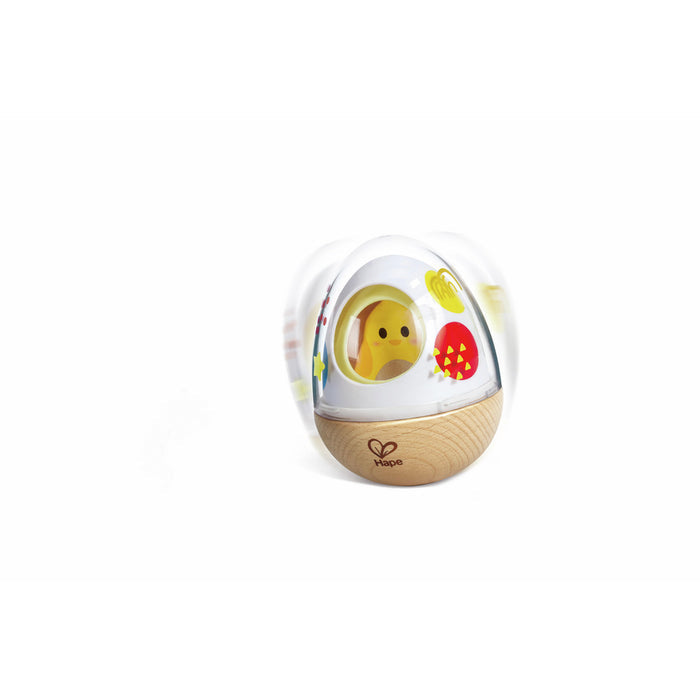 Egg-shaped wobble toy with a wooden base, white shell, and yellow chick inside, shown rocking back and forth.