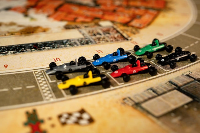 Six colorful vintage race car miniatures lined up on a numbered board game track with illustrated grid spots.