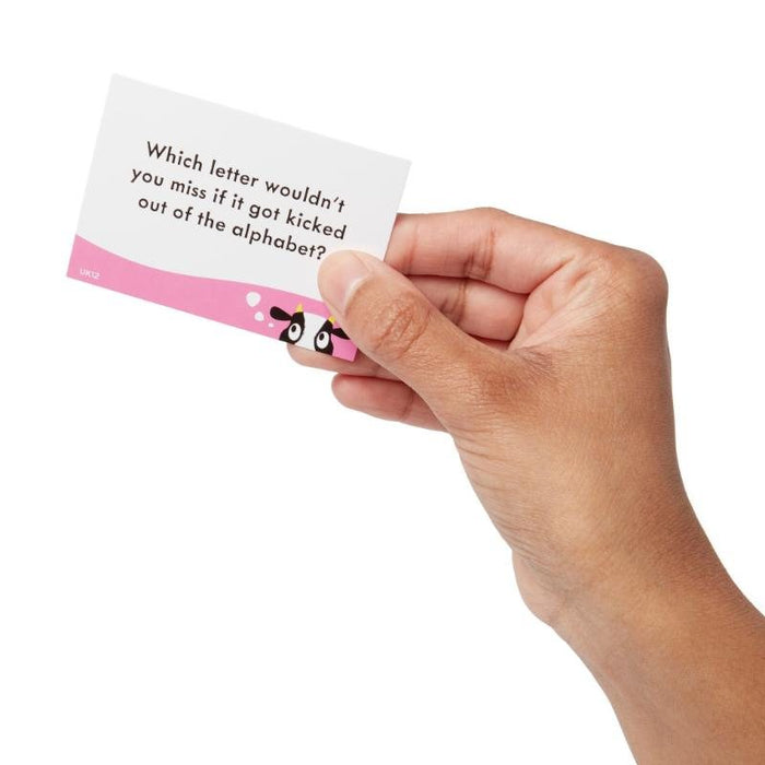 Hand holding a game card with a pink cow border. Text: Which letter wouldn't you miss if it got kicked out of the alphabet?