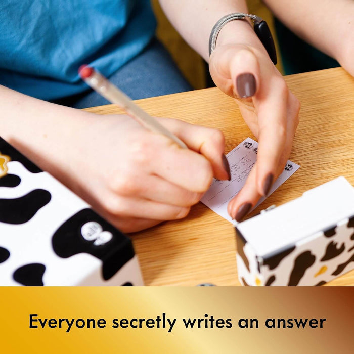 Close-up of hands writing a secret answer on a notepad slip next to cow-print boxes on a wooden table.