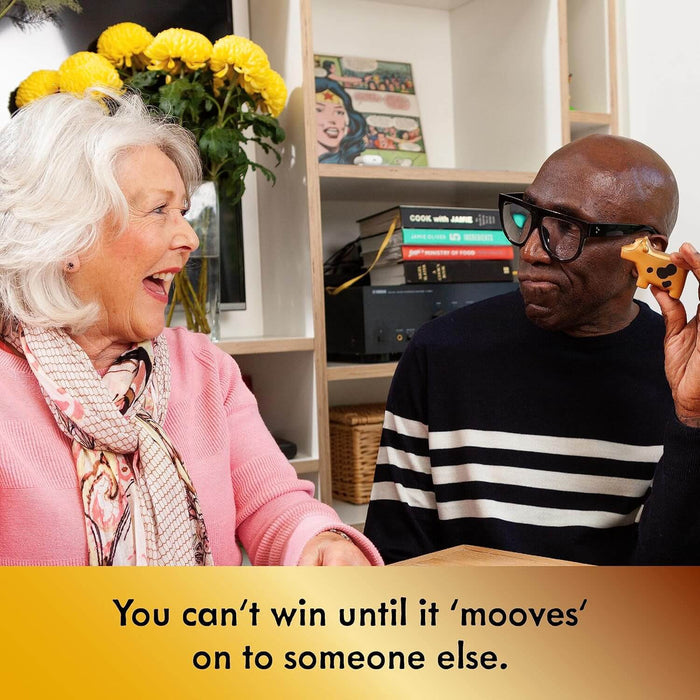 Older man in glasses holds orange cow toy to ear as woman laughs. Text: You can't win until it 'mooves' on to someone else.