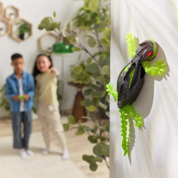 Robotic black and neon green gecko with glowing red eyes climbing a wall as children watch in the background.