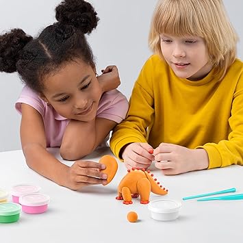Two children sculpting an orange clay dinosaur with colorful modeling clay tubs and tools on a white surface.