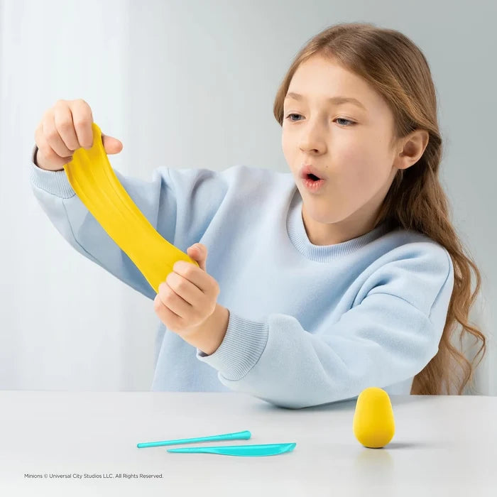 A girl stretching bright yellow modeling clay next to turquoise tools and a yellow clay egg on a white table.