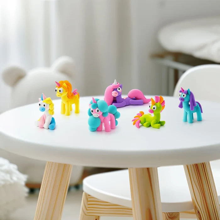 Six colorful clay unicorn figures in vibrant colors and poses arranged on a white table in a bright playroom.