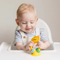 Baby playing with a yellow silicone lion toy featuring colorful rings and a suction base on a white high chair tray.