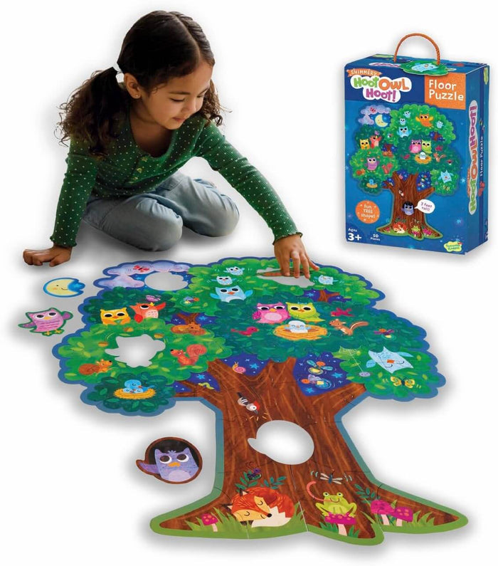 Child assembling a large tree-shaped floor puzzle featuring colorful owls and forest animals next to the blue product box.
