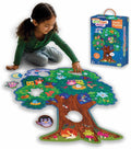 Child assembling a large tree-shaped floor puzzle featuring colorful owls and forest animals next to the blue product box.