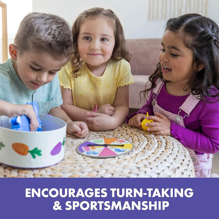 Three children play a game using a blue bunny squeezer, colorful spinner, and illustrated bowl on a woven table.
