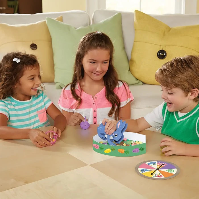 Kids use blue bunny-shaped tweezers to collect colorful carrots into purple baskets during a tabletop game.