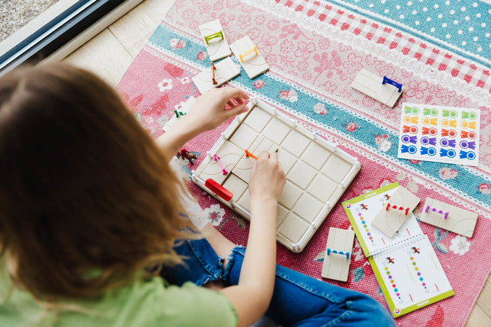 A child plays with a Horse Academy logic game on a colorful rug, arranging obstacle puzzle pieces on a grid board.