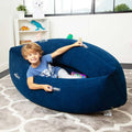 Child sitting in a blue inflatable peapod-shaped sensory pod with clear handles on a patterned gray rug.