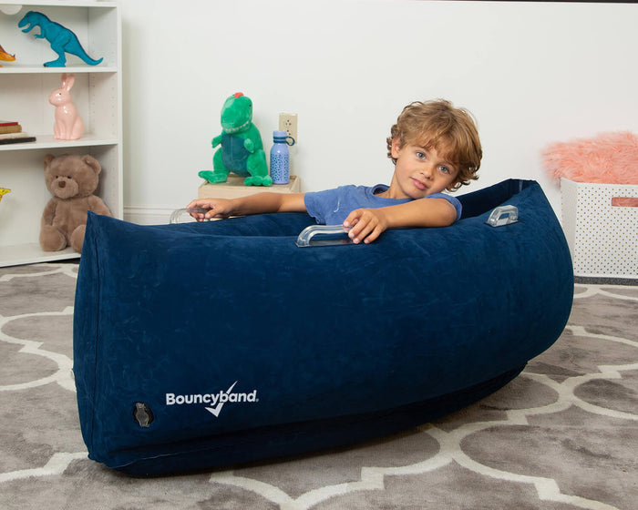 Child sitting in a blue inflatable peapod-shaped sensory canoe with clear side handles and white Bouncyband logo.