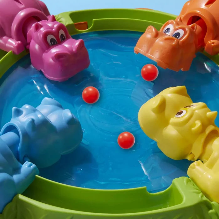Pink, orange, yellow, and blue plastic hippos snap at red marbles on a circular blue and green game board.