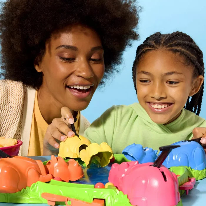 Woman and child smile while playing with pink, blue, yellow, and orange plastic hippos on a green board.