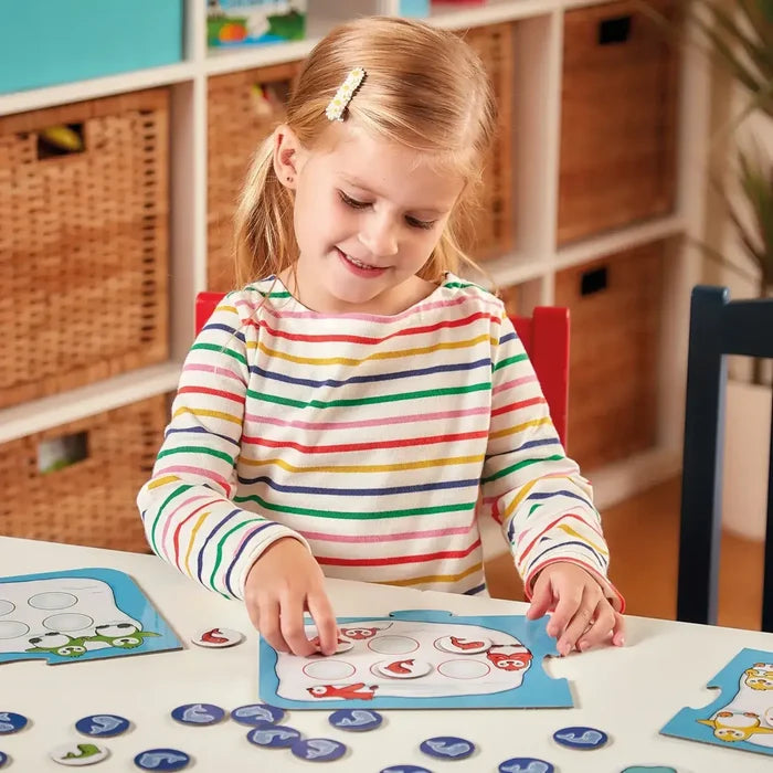 Child in a striped shirt placing colorful round fish tokens onto blue penguin-themed game boards.