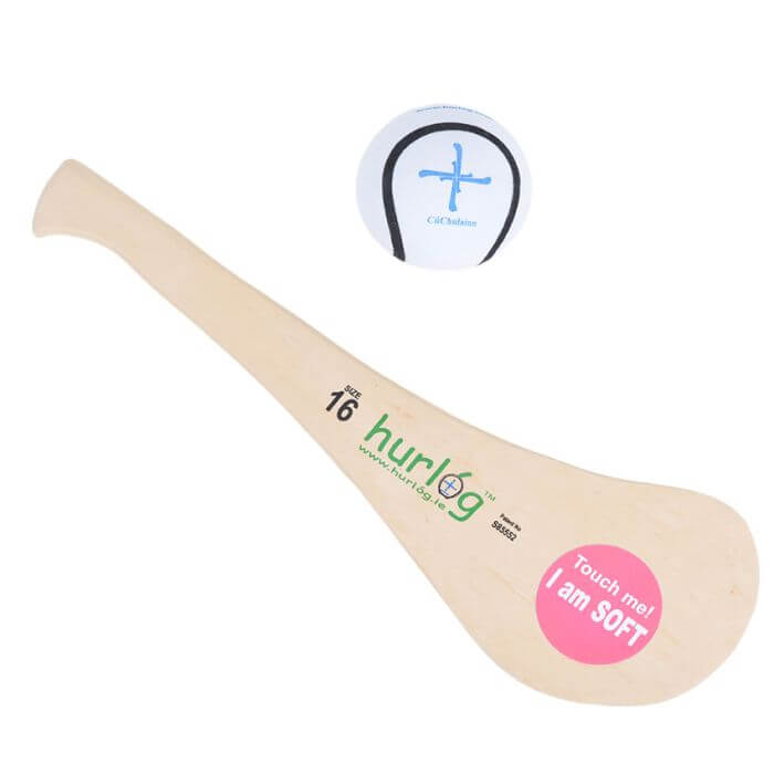 Soft beige hurley stick with green logo and pink sticker, shown with a white ball with blue cross markings.