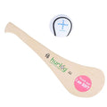 Soft beige hurley stick with green logo and pink sticker, shown with a white ball with blue cross markings.