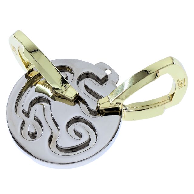 Circular silver metal puzzle with maze-like grooves and two interlocking gold-colored pieces.