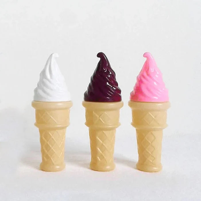 Three toy ice cream cones with tan waffle bases and glossy swirled tops in white, dark purple, and pink.