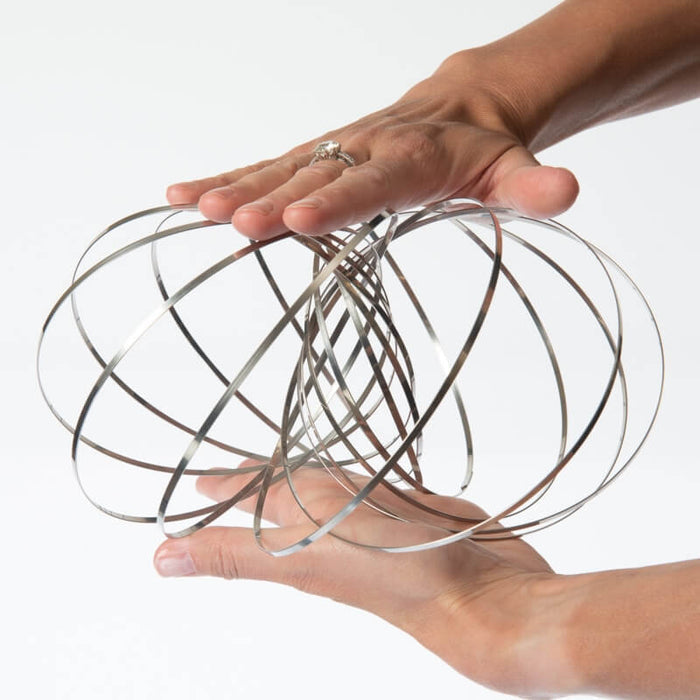 Two hands holding a spherical kinetic toy made of thin, interlocking shiny silver metal rings.