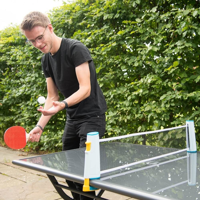 Man using a portable blue and white table tennis net clamped to a glass table with a red paddle and ball.