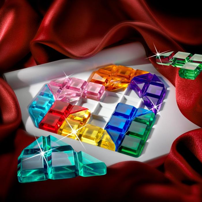 Colorful jewel-toned 3D puzzle pieces in a heart-shaped tray on a red satin backdrop.