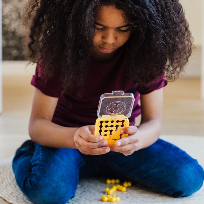 Child playing with a yellow IQ Mini logic puzzle featuring a clear flip-top lid and small yellow game pieces.