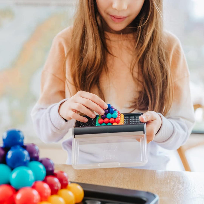 Girl building a 3D pyramid of colorful connected spheres on a black travel case board with a clear lid.